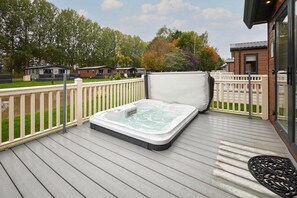 Ein Whirlpool auf einer Holzterrasse mit einem weißen Zaun und Blick auf Häuser im Hintergrund.
