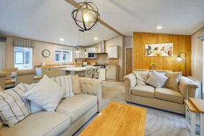 A modern living room with a sofa, a coffee table, and a kitchen area in the background. - Host Stay Water s Edge Lodge (York)