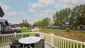 A deck with a round table and chairs, overlooking a river and a row of houses. - Host Stay Water s Edge Lodge (York)