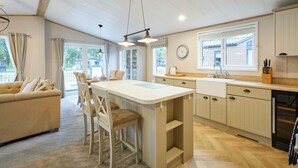 A modern kitchen with a central island, wooden cabinets, and a dining area with a sofa and chairs. - Host Stay Water s Edge Lodge (York)