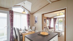 Een moderne keuken met een houten aanrecht, een eettafel en stoelen. Er is een raam met gordijnen, een plafondlamp en uitzicht op buiten.