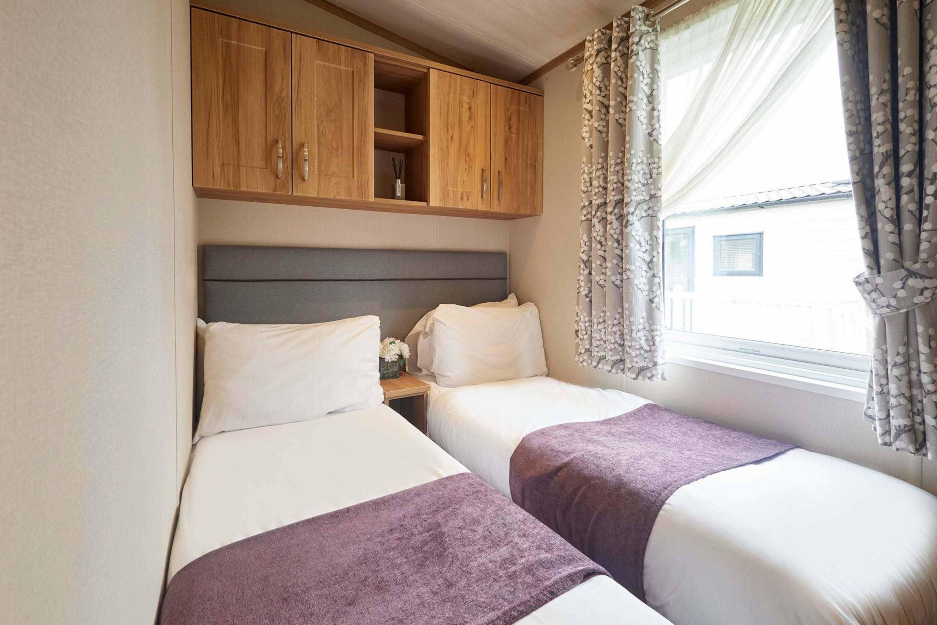 Un dormitorio con dos camas, armarios de madera arriba y una ventana con cortinas.