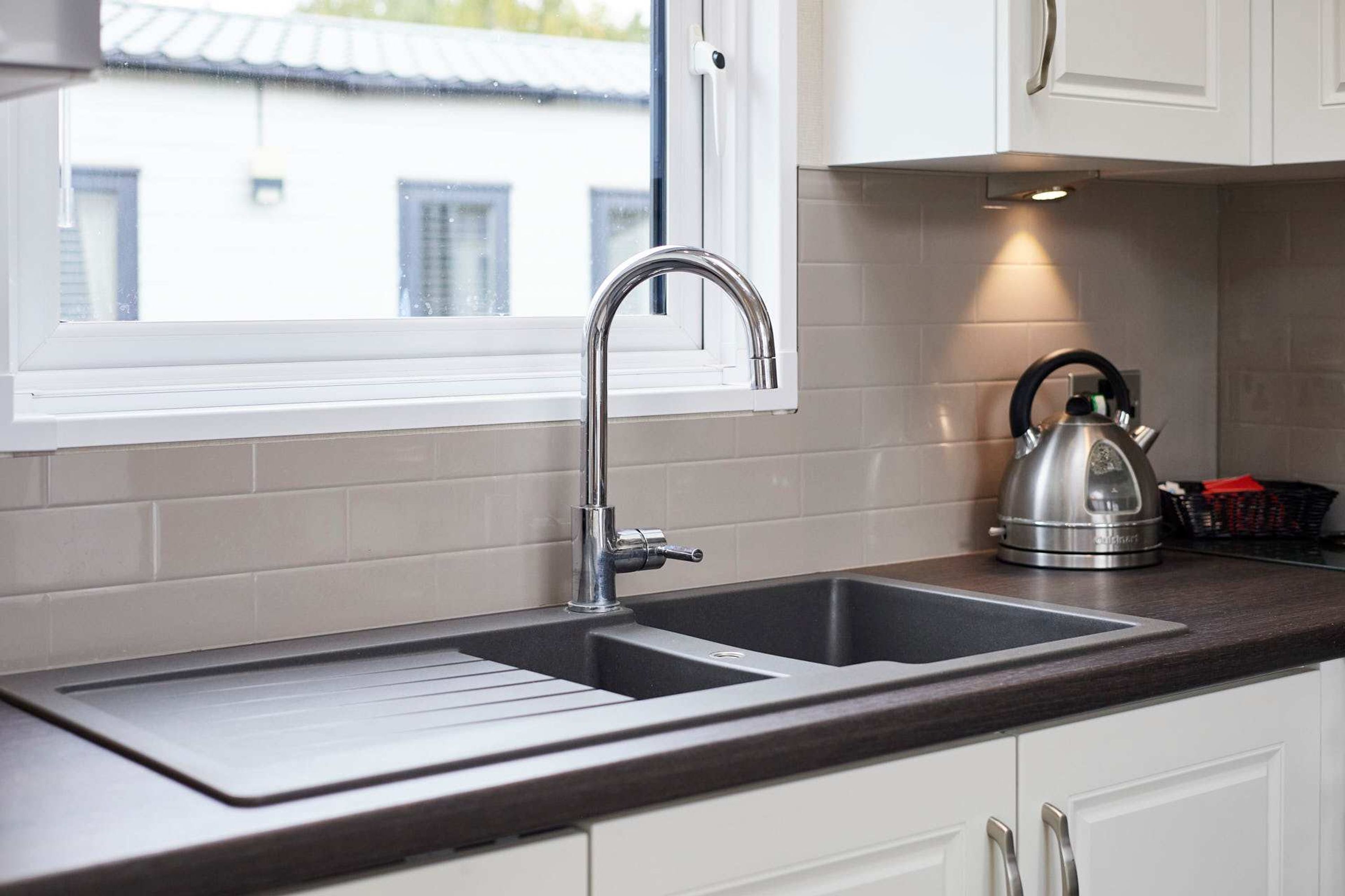 A kitchen with a double sink, a kettle, and a window with a view of buildings.