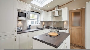 Een moderne keuken met witte kasten, een ingebouwde magnetron, een gasfornuis en een dakraam.
