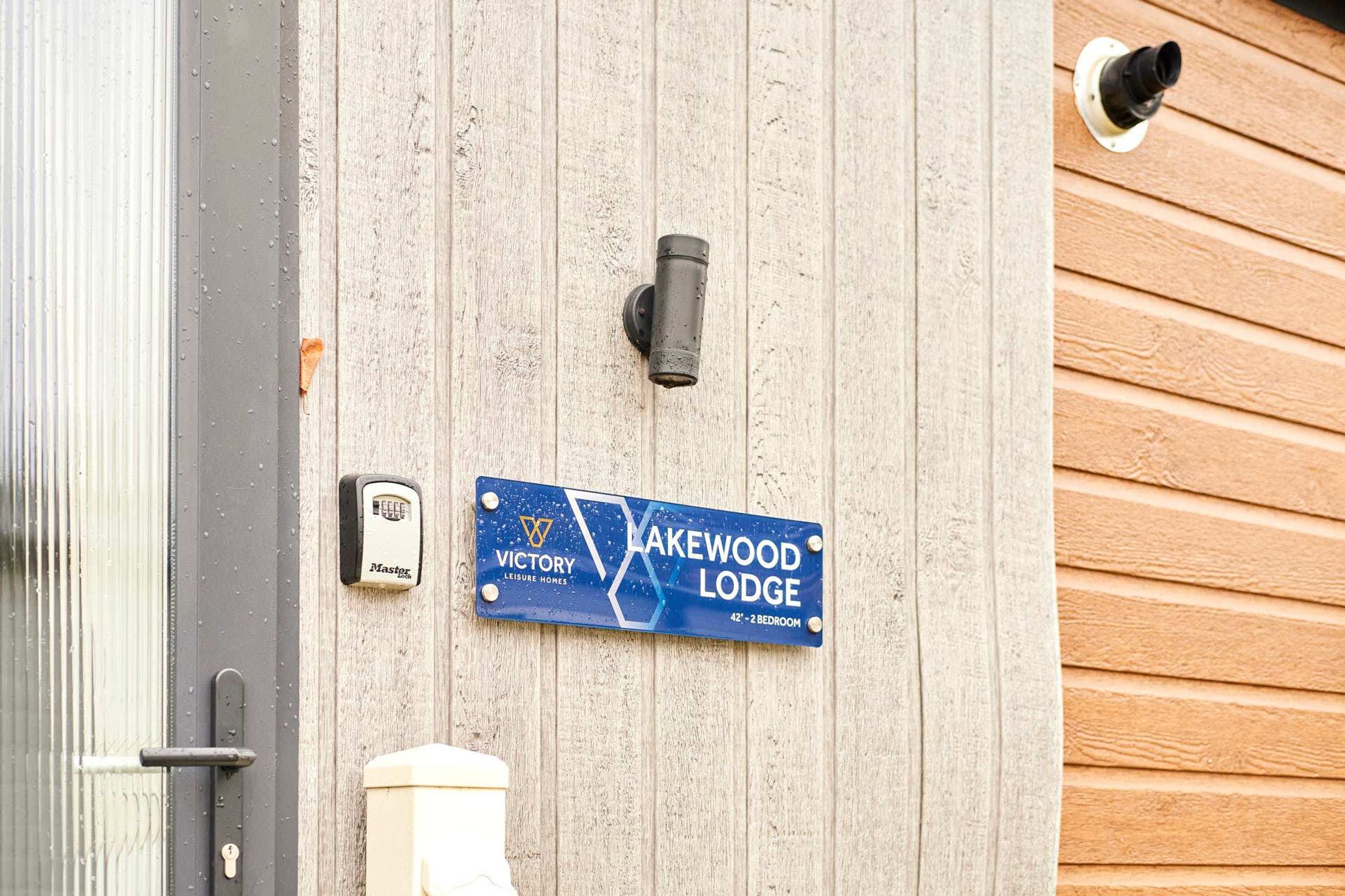 A door with a security lock, a peephole, and a blue sign indicating 'Lakewood Lodge' with 'Leisure Homes' branding.