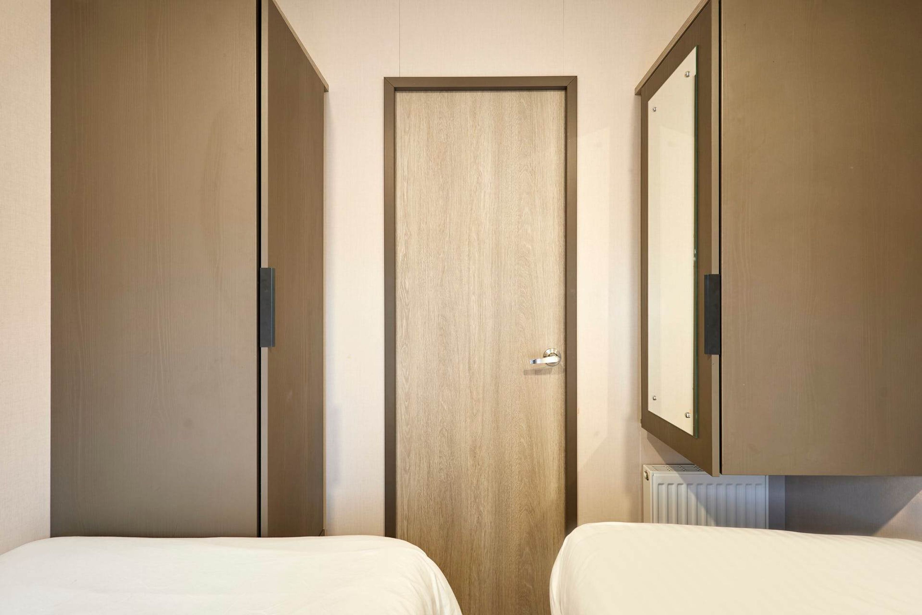 Ett hotellrum med två sängar, en trädörr och en stor spegel.