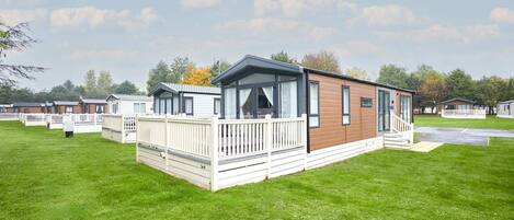 A mobile home with a deck, a porch, and a fenced yard.