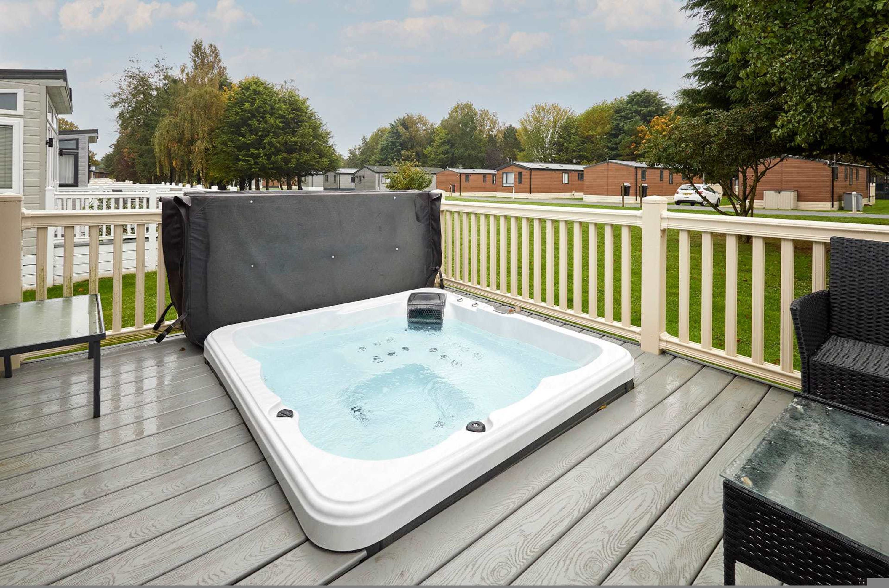 Een jacuzzi op een houten terras, met een witte omheining en uitzicht op woongebouwen.