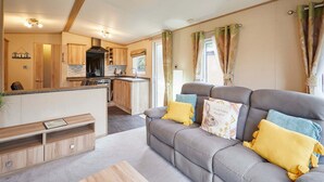 A modern living room with a grey sofa, wooden storage unit, and a kitchen area in the background. - Host Stay Brooksbank Lodge (York)