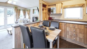 A compact kitchen with a dining area, wooden cabinets, a microwave, and a window with curtains. - Host Stay Brooksbank Lodge (York)