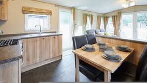 A compact kitchen with a sink, wooden cabinets, a dining table set with plates, and a window with curtains. - Host Stay Brooksbank Lodge (York)