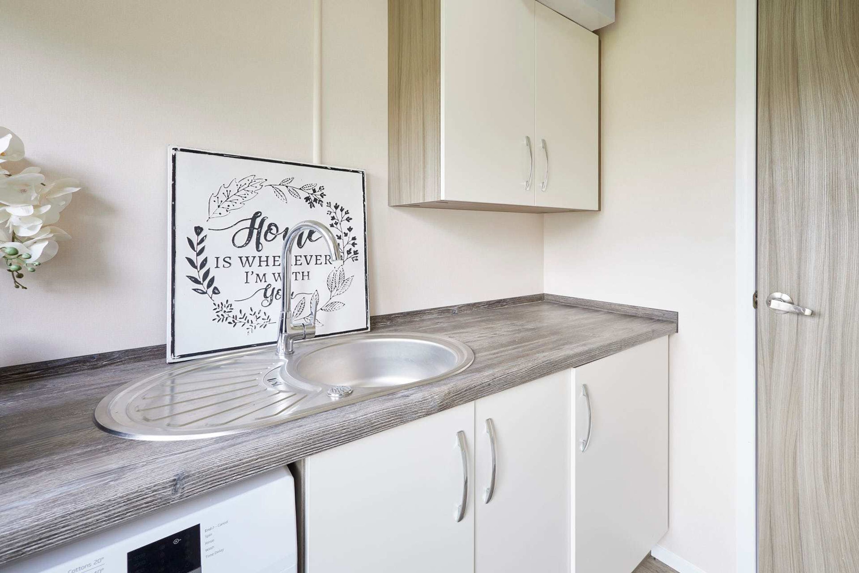 A kitchen with a white countertop, a stainless steel sink, and a cabinet above.