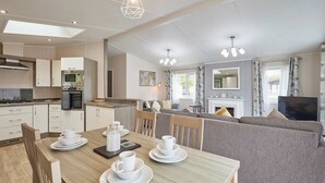 Una cocina moderna con electrodomésticos integrados, un comedor con mesa dispuesta para cuatro personas y una sala de estar con sofá y televisor.