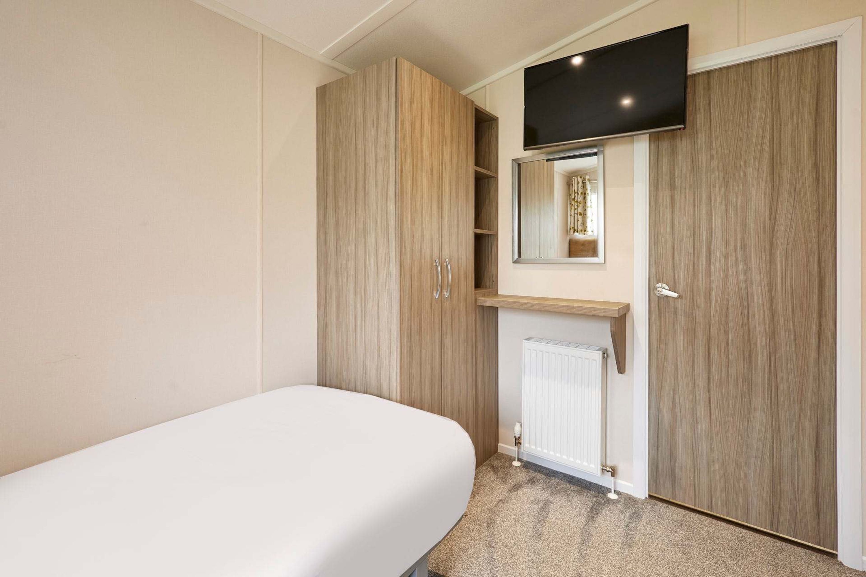 A bedroom with a bed, a wardrobe, a television mounted above a mirror, and a radiator.
