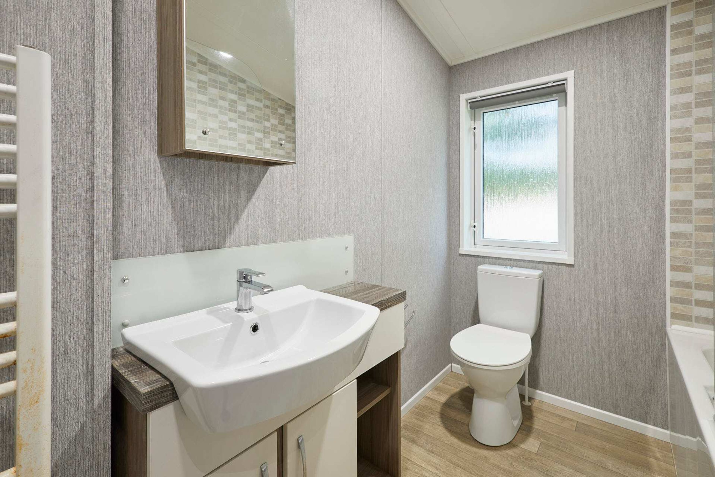 A modern bathroom with a white sink, a toilet, and a window.