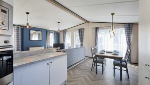 Moderni keittiö, jossa on keskeinen saareke, ruokailutila pöytineen ja tuoleineen sekä olohuone, jossa on sohva.