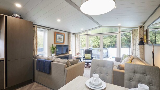 A modern, well-lit room with a sofa set, a dining table with plates and cups, and a television. - Host Stay 23 Sandy Lane (York)