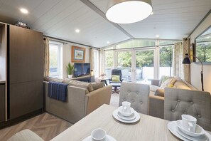 A modern, well-lit room with a sofa set, a dining table with plates and cups, and a television. - Host Stay 23 Sandy Lane (York)