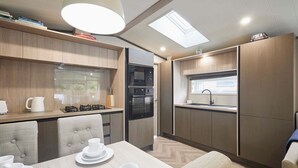 A compact kitchen with modern appliances, a dining area with a table set for two, and a window providing natural light. - Host Stay 23 Sandy Lane (York)