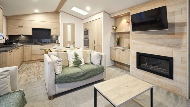 A modern kitchen with built-in appliances, a dining area with a sofa and table, and a fireplace. - Host Stay Fir Tree Lodge (York)
