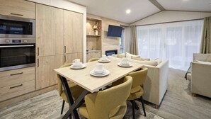 A modern kitchen with built-in appliances, a dining area with a table set for four, and a living area with a sofa and TV. - Host Stay Fir Tree Lodge (York)