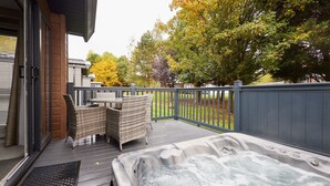 An outdoor deck with a hot tub, wicker chairs, and a table. - Host Stay Fir Tree Lodge (York)