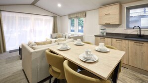 A modern kitchen with wooden cabinets, a dining table set with white plates and cups, and a large window with blinds. - Host Stay Fir Tree Lodge (York)
