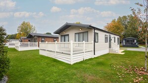 A mobile home with a deck and a small porch, surrounded by a grassy lawn and trees. - Host Stay Primrose Lodge (York)