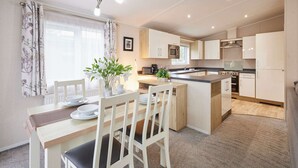 A modern kitchen with white cabinetry, a central island, and a dining area with a table and chairs. - Host Stay Primrose Lodge (York)