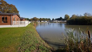 A lakeside property with a wooden cabin, a grassy lawn, and a calm lake. - Host Stay Primrose Lodge (York)