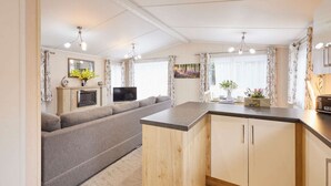A modern living room with a sofa, a TV, and a kitchen area with a wooden counter and cabinets. - Host Stay Primrose Lodge (York)
