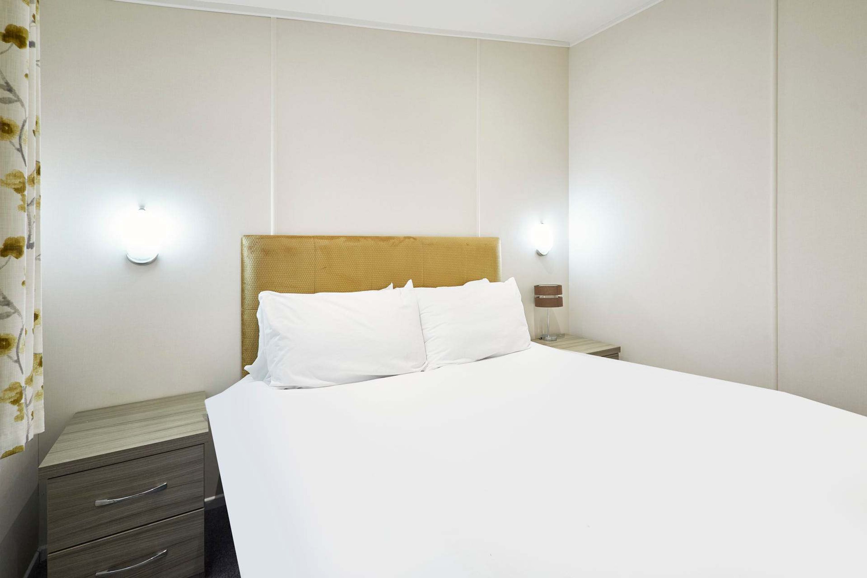 Habitació d'hotel amb un llit, una tauleta de nit i dues làmpades penjades a la paret.