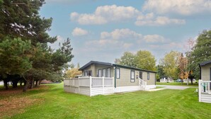 Une maison mobile de plain-pied dotée d’une terrasse clôturée, entourée d’une pelouse bien entretenue et d’arbres.