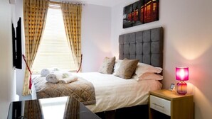 Una habitación de hotel con una cama, una mesita de noche con lámpara, un televisor y una ventana con cortinas.