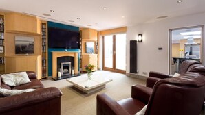 Una sala de estar moderna con chimenea, sofás de cuero, un televisor de pantalla plana y una estantería.
