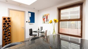 Un comedor moderno con una mesa de granito, sillas negras, una estantería de madera para vinos, un tablón azul de anuncios y un cuadro en la pared.