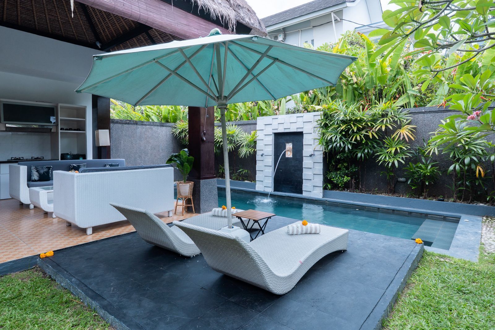 Uma área de estar moderna ao ar livre, com piscina, espreguiçadeiras e um espaço coberto para sentar.