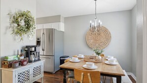 A dining area with a wooden table set for four, a chandelier, and a decorative wall hanging. - Howdy Hang Out - Cozy, Cute And Comfortable House! 2 Bedroom Home (Bryan)