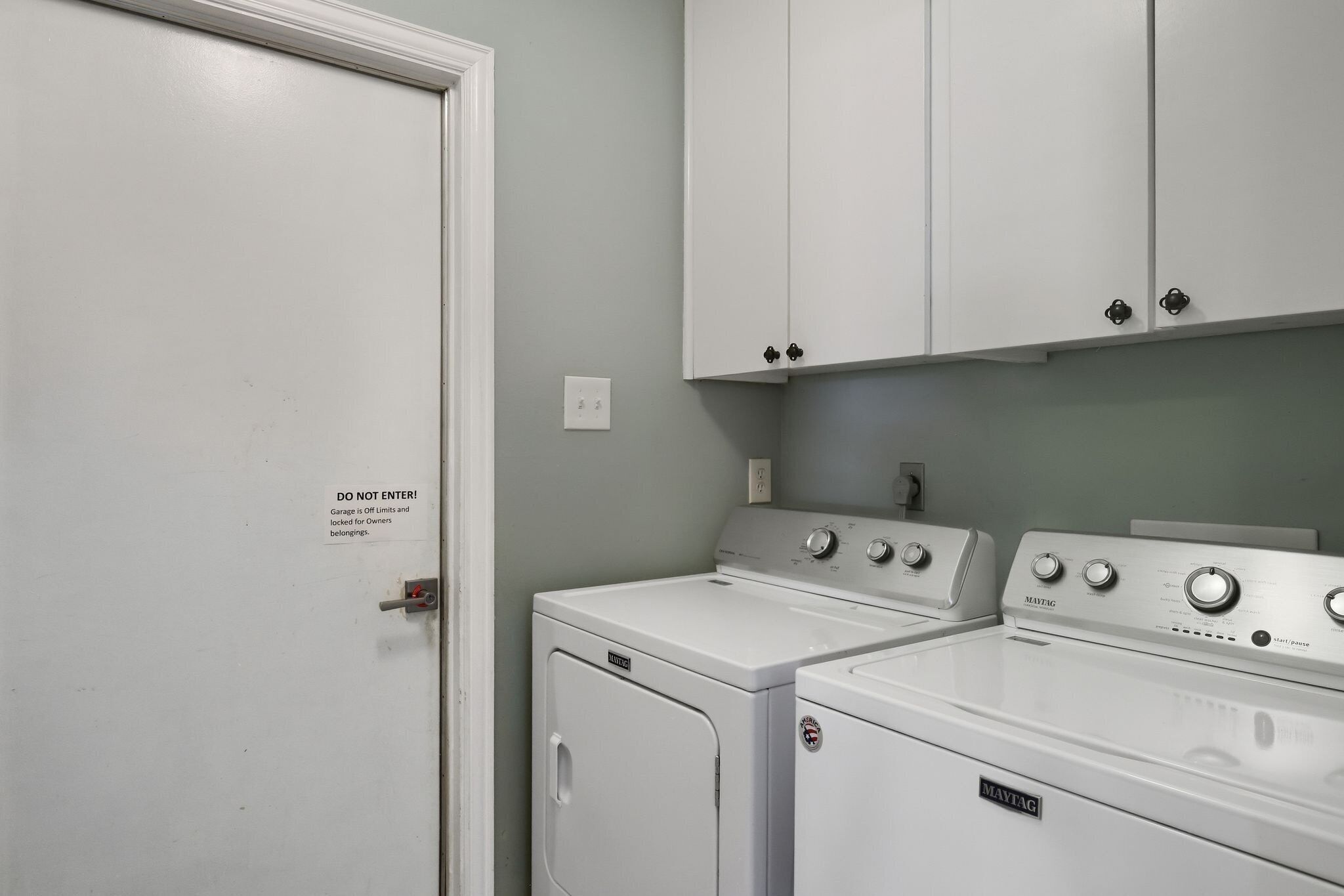 A laundry room with two white washing machines and a closed door with a 'DO NOT ENTER' sign.
