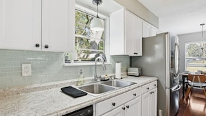 A modern kitchen with white cabinets, a stainless steel refrigerator, a double sink, and a window providing natural light. - Howdy Hang Out - Cozy, Cute And Comfortable House! 2 Bedroom Home (Bryan)