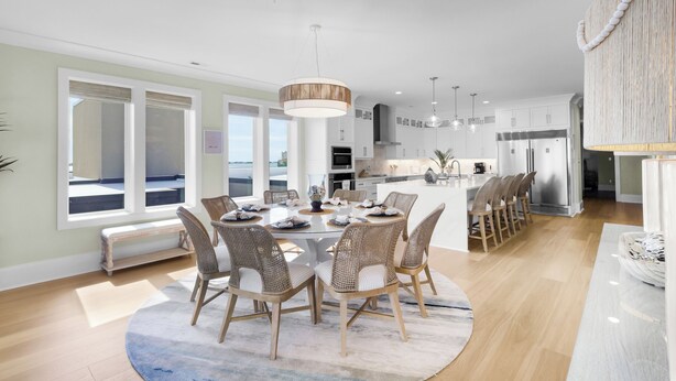 Une cuisine moderne avec des meubles blancs, un îlot central et un coin repas comprenant des chaises en osier et une table ronde.
