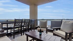 Un balcon avec vue sur l’eau, agrémenté de chaises et d’une table, et une bouteille de champagne.