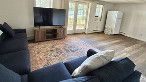 Ett rymligt vardagsrum med en stor hörnsoffa, en platt-TV och ett kylskåp.