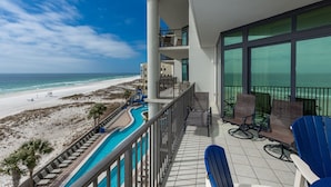 Een balkon met uitzicht op het strand en de oceaan, een zwembad met ligbedden en een eethoek met tafels en stoelen.