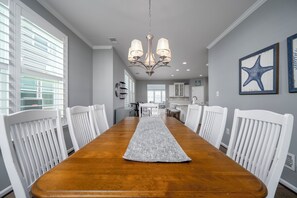 A dining room with a wooden table, white chairs, a chandelier, and artwork on the walls. - Spacious 4 bed, 3.5 bath townhome located in Ocean View Beach Club; community pool, fitness center, shuttle, playground, sauna, Free WIFI (Ocean View)