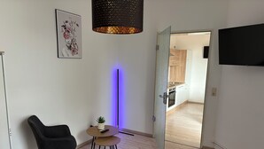Un salón moderno con una silla negra, una mesita redonda con una planta, una alfombra negra y un televisor montado en la pared.