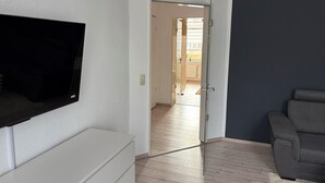 Una sala de estar moderna con un televisor de pantalla plana montado en la pared, un sofá gris y piso de madera.