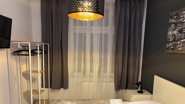 Un dormitorio con una cama, una mesita de noche, una lámpara colgante, un armario y cortinas de gasa.