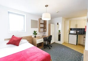 A hotel room with a bed, desk, chair, kitchenette, and a window. - Student Only Luxury Apartment at Islington Near Emirates Stadium (London)