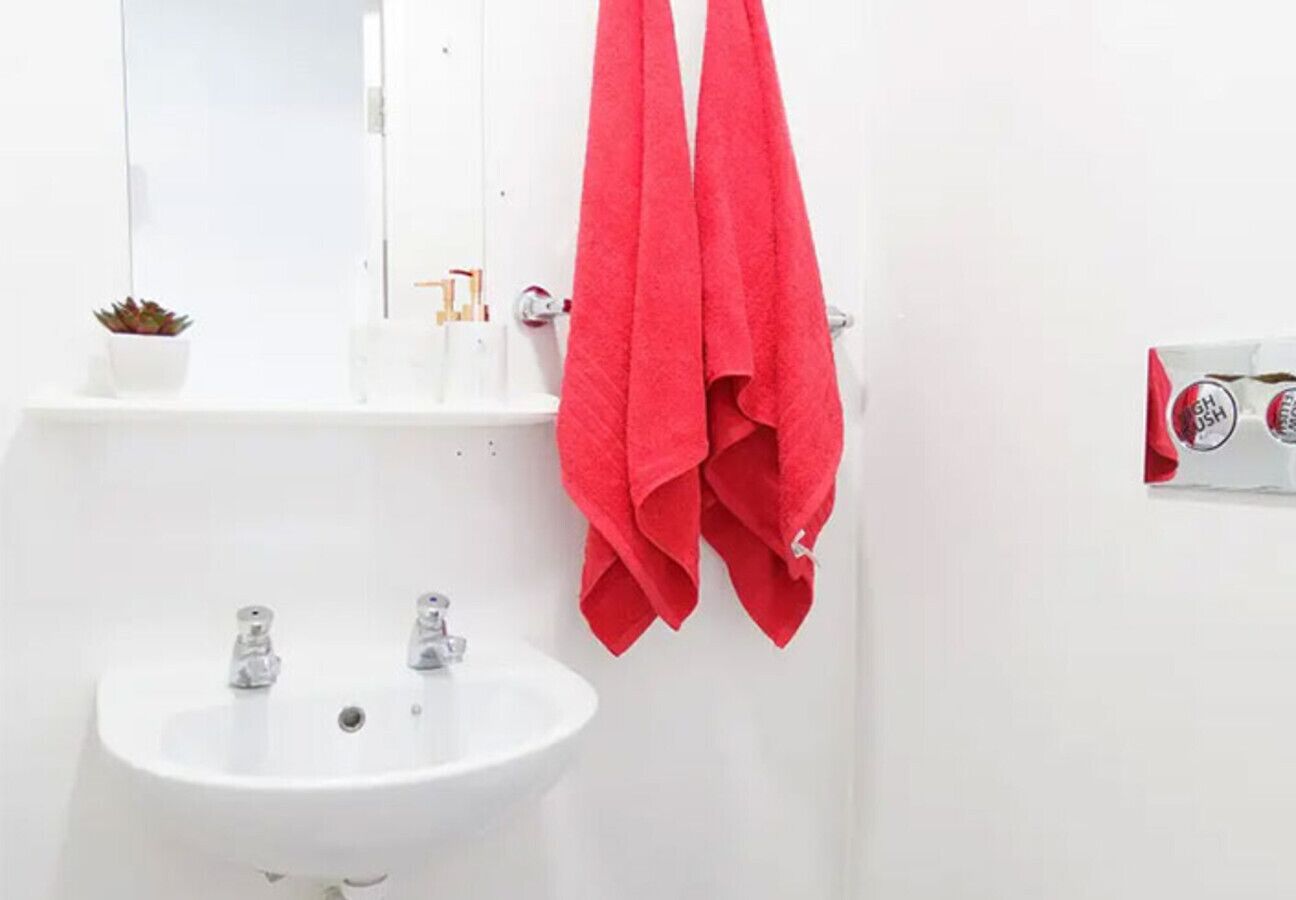 A bathroom with a white sink, two faucets, and a mirror. There are two red towels hanging on a towel rack.